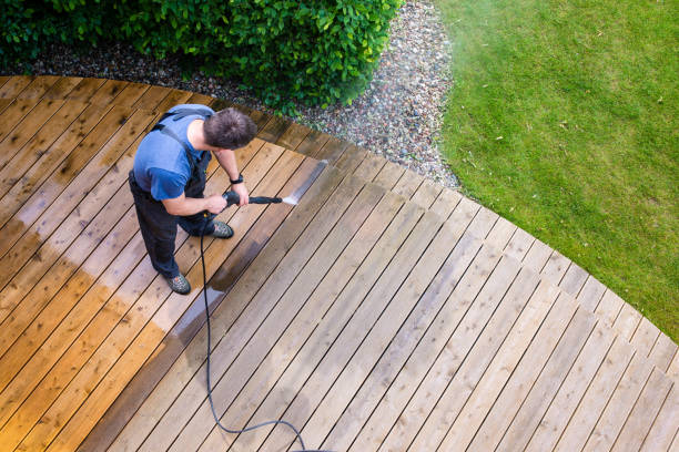 man power washing an outdoor wooden terrace, half of the deck has been cleaned, while the other half has not